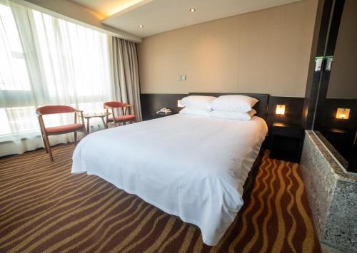Habitación de hotel con cama grande con sábanas y almohadas blancas. en J-Grand Hotel en Jeju