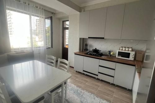 eine Küche mit weißen Schränken, einem Tisch und einer Mikrowelle in der Unterkunft Apartament Manasa in Bischkek