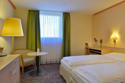 a hotel room with two beds and a desk and a window at PLAZA INN Leonberg in Leonberg