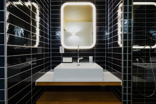 baño con lavabo blanco y paredes de azulejos negros. en Apartments De Hallen en Ámsterdam