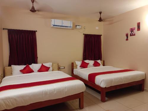 two beds in a hotel room with red pillows at Paradise Breeze Inn in Kottakupam