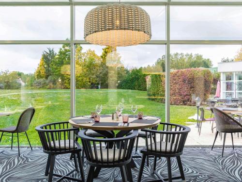サン・ピエール・デュ・ペレにあるNovotel Senart Golf De Greenparcの大きな窓のある客室で、テーブルと椅子が備わります。