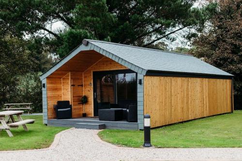 a small wooden shed with a table and a picnic table at Riverside Retreats - Steamers Meadow in Gwinear