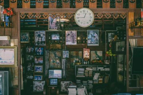 eine Uhr an einer Wand mit Bildern und Büchern in der Unterkunft Ban Mae Arom in Amphawa