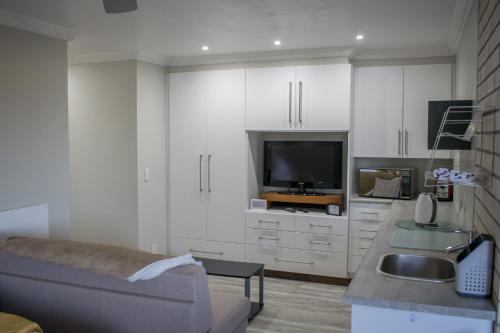 a kitchen with white cabinets and a couch and a tv at Vista Views in Herolds Bay
