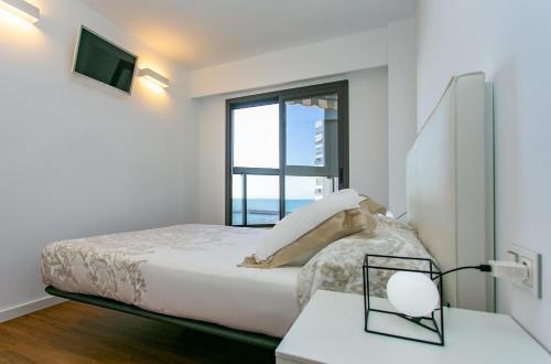 a white bedroom with a bed and a window at Cullera Beach Apartment Espacio in Cullera