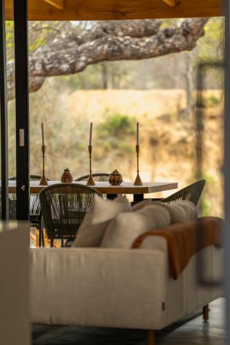 a table with chairs and a white couch in front of a window at Nomads Den Safari Villas - Heated Pools and Riverbed views in Hoedspruit