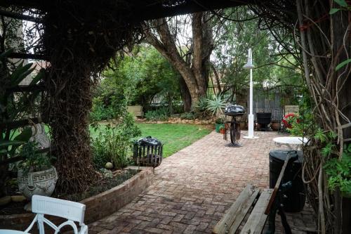 a garden with a brick walkway with benches and trees at Outentique Accommodation in Oudtshoorn