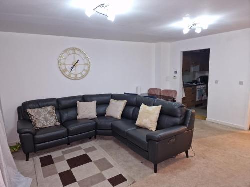 a black couch in a living room with a clock on the wall at KO 3 bed house in Kent