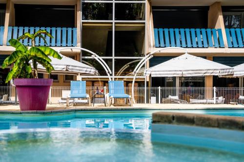 - une piscine avec 2 chaises bleues et des parasols dans l'établissement Hotel Logis Lacotel, à Hossegor