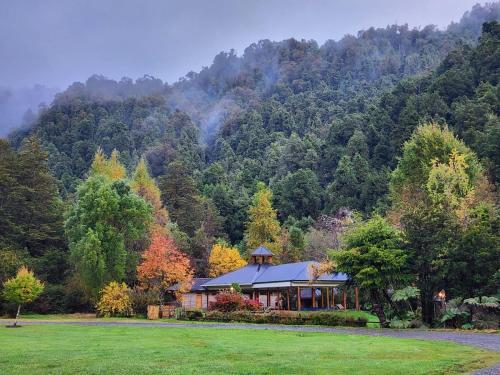 a house in the middle of a field in front of a mountain at El Pangue Lodge in Puerto Puyuhuapi