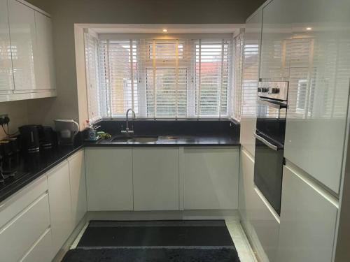 a kitchen with white cabinets and a sink and a window at Lovely Detached house in lovely location in West Drayton