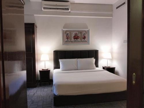 Times Square Service Suites Kuala Lumpur في كوالالمبور: غرفة نوم بسرير مع شراشف بيضاء ومصباحين