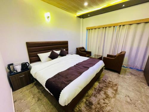 Hotel candlewood Shimla في شيملا: غرفة نوم بسرير كبير وكرسيين