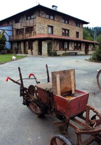 un viejo carro oxidado delante de un edificio en Aristieta, en Ajangiz