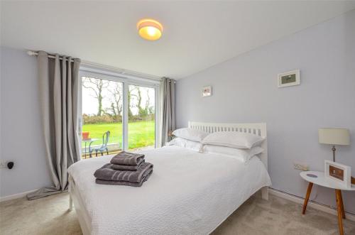 a bedroom with a white bed and a large window at Gwyllt Cottages in Dwyran