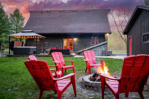 four red chairs around a fire pit in front of a house at Cozy Cabin Inn in Owen Sound