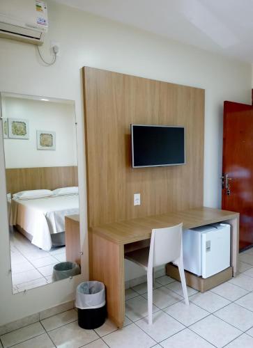 a room with a desk with a television and a bed at Tawfiqs Hotel in Barra do Garças