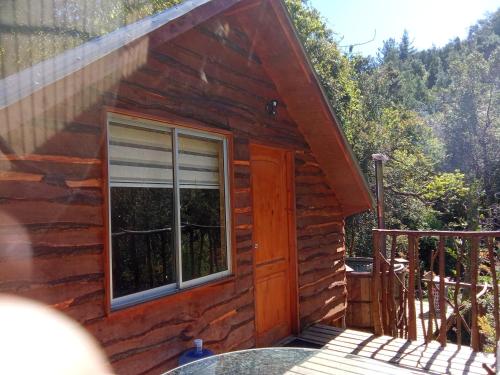 une cabane en rondins avec une fenêtre et une terrasse dans l'établissement Refugio y Tinaja Curiñanco, à Valdivia