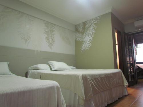 um quarto com duas camas com lençóis brancos e folhas de palmeira na parede em Pousada Villa Guimaraes em Chapada dos Guimarães