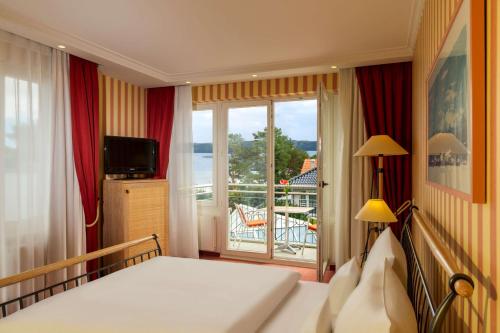 a bedroom with a bed and a view of a balcony at Dorint Strandhotel Binz/Rügen in Binz
