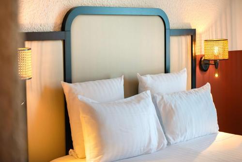 a bed with a blue headboard with white pillows at Best Western Porte du Forez in Andrézieux-Bouthéon