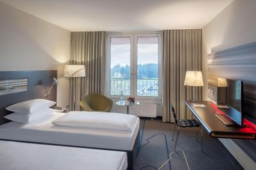 a hotel room with two beds and a desk and a television at Dorint Am Nürburgring Hocheifel in Nürburg