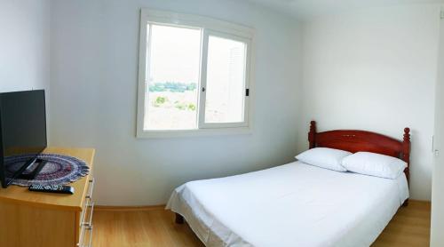a white bedroom with a bed and a window at Apartamento em Bento Gonçalves-RS in Bento Gonçalves