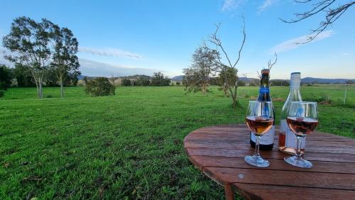 Dois copos de vinho e uma garrafa numa mesa de madeira. em Vacy Hunter Valley Lodge em Vacy