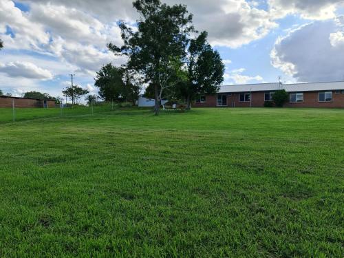a large green field with a building and a tree at Vacy Hunter Valley Lodge in Vacy