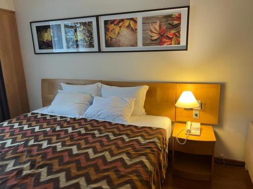 um quarto de hotel com uma cama com um candeeiro e fotografias na parede em Hotel Alphaville em Barueri