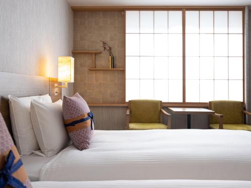 a bedroom with a white bed with two chairs at Mitsui Garden Hotel Kyoto Station in Kyoto