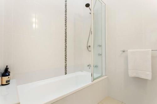 a white bathroom with a shower with a mirror at A Perfect Stay - Beach House at Tallows in Byron Bay