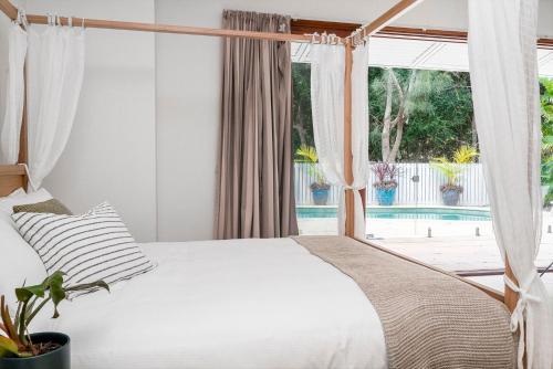 a bedroom with a white bed and a window at Beachcomber Blue - beachfront villa with pool in Byron Bay