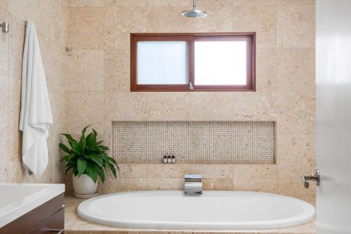 a white tub in a bathroom with a window at Beachcomber Blue - beachfront villa with pool in Byron Bay