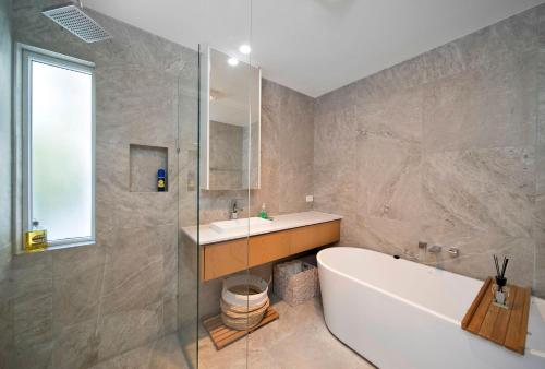 Un baño con bañera, lavabo y ducha. en Byron Sunrise - 4 BR retreat with heated pool, en Byron Bay
