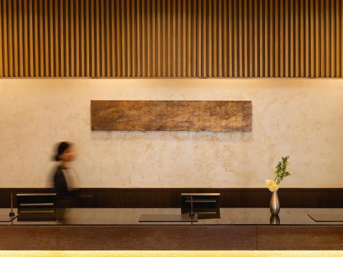 a woman walking through a waiting room with two benches at Mitsui Garden Hotel Kyoto Sanjo in Kyoto