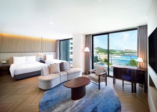 ソギポにあるParnas Hotel Jejuのベッド、ソファ、テーブルが備わるホテルルームです。