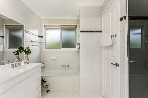 Baño blanco con bañera y lavamanos en A Perfect Stay - Tradewinds 4 en Bangalow