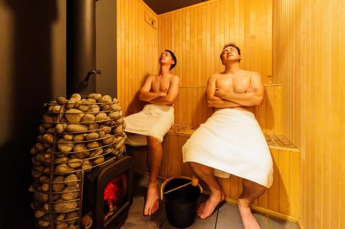 Dois homens sentados numa sauna com os braços cruzados. em Hakuba Aurora Chalet by Jade Group em Hakuba