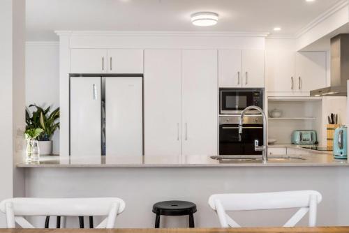 a white kitchen with white cabinets and black appliances at Ocean Walk - Villa near Main Beach in Byron Bay