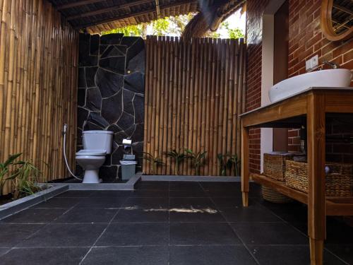 a bathroom with a toilet and a stone wall at RaCottage Mandalika in Kuta Lombok