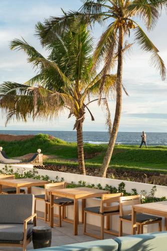 a patio with tables and palm trees and the ocean at The Charleston in Galle