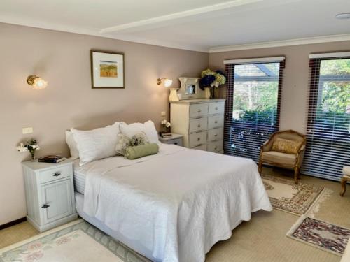 ein Schlafzimmer mit einem weißen Bett und einem Stuhl in der Unterkunft French Provincial The Garden Suite at Chapmans incl Breakfast & Golf in Moss Vale