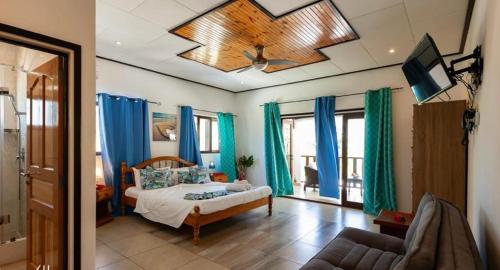 1 dormitorio con 1 cama con cortinas azules y TV en Hyde-Tide Guesthouse, en La Digue