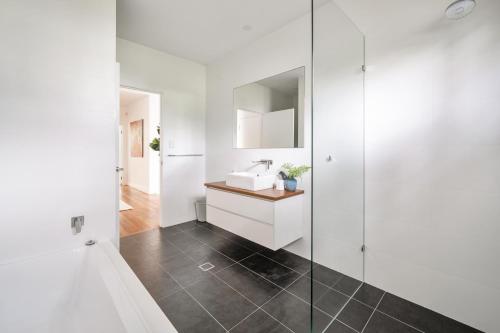 a white bathroom with a sink and a mirror at 'rockpool' - Direct Beach Access in Coledale