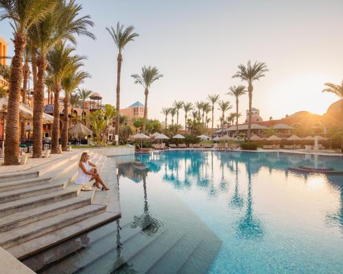 a woman sitting on a bench next to a pool at a resort at The Grand Resort in Hurghada