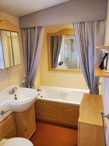 a bathroom with a sink and a tub and a mirror at 6 Berth Central heated on The Chase (Balmoral) in Ingoldmells