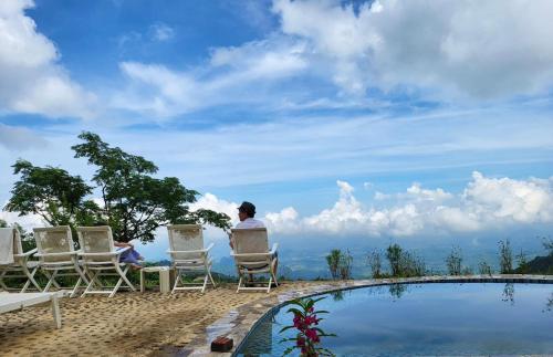 um homem sentado em cadeiras ao lado de uma piscina em Mường Ecolodge Hòa Bình em Hòa Bình