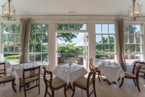 a dining room with white tables and chairs and large windows at Bartley Lodge Hotel in Lyndhurst